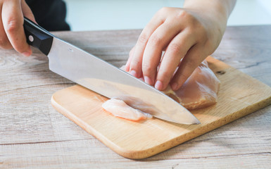 Hand cutting Chicken on wooden chopping board.