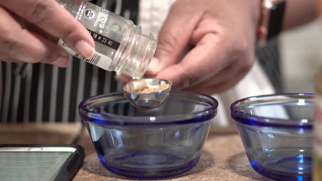 Close Up, hands pouring ground cumin into measuring spoon over blue bowl