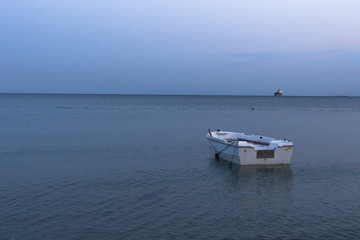 Sea trading port. White boat on the sea in the evening. Water surface. Cargo ship. Fishing boat. Ship in the harbor. Moored boat. Evening seascape.