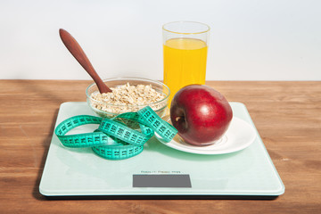 The concept of healthy diet, fitness and weight loss. Scales, measure tape, oatmeal, apple, a glass of juice on the table. 