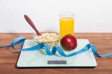 The concept of healthy diet, fitness and weight loss. Scales, measure tape, oatmeal, apple, a glass of juice on the table. 