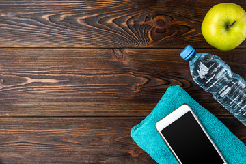 Mobile phone, apple, bottle of water and towel on dark wooden background. 