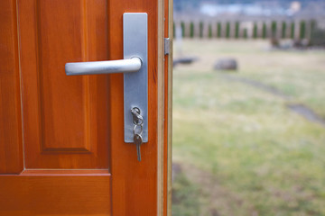 Open wooden door with keys in keyhole on defocused landscape background.