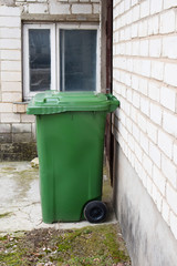 Green plastic bin for waste garbage outdoors next to brick wall of building.