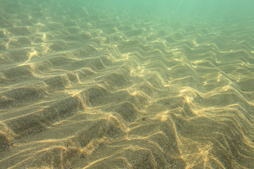 Underwater photo, sun shining on sea floor in shallow water, sand forming 