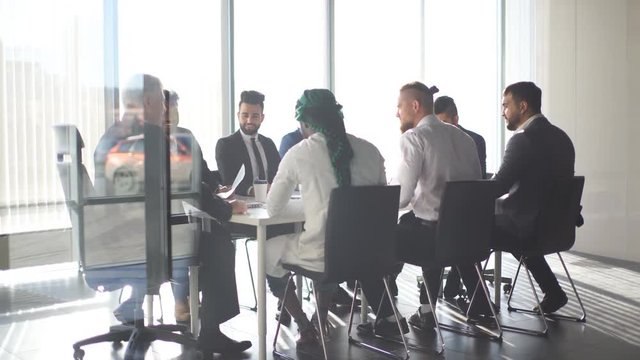 Multiracial team of business partners of different age interacting in boardroom of modern spacious and well-lit office, being viewed through transparent glass wall.