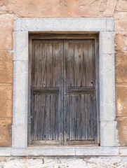 Old wooden brown window on stone wall in Greece.