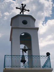 Beautiful white chapel bell tower with metal cross and blue railed balcony under dramatic sky with clouds.