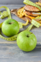 green apples on the background of a burger and fries. Sewing Tape Measures on the food. concept of opposition  healthy food and junk food. selective focus