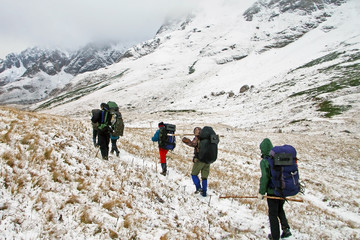 group of tourists with equipment and backpacks climb to the snowy peaks of the mountain