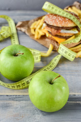 green apples on the background of a burger and fries. Sewing Tape Measures on the food. concept of opposition  healthy food and junk food. selective focus