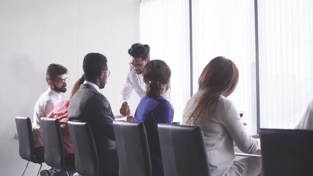 Indian man handing out paper tests to his international co-workers during corporate training meeting. Educational Concept.