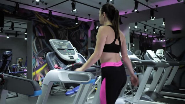 inspiring backside view brunette girl in top and leggings walks quickly on modern gray treadmill in gym