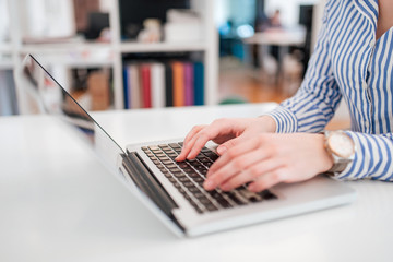 Unrecognizable woman wearing blouse with stripes working on laptop, close-up.