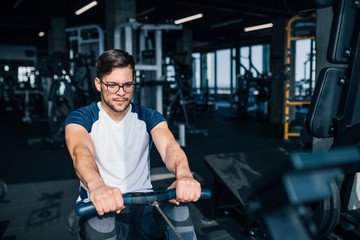 Fototapeta na wymiar Handsome man training on row machine in the gym, front view.