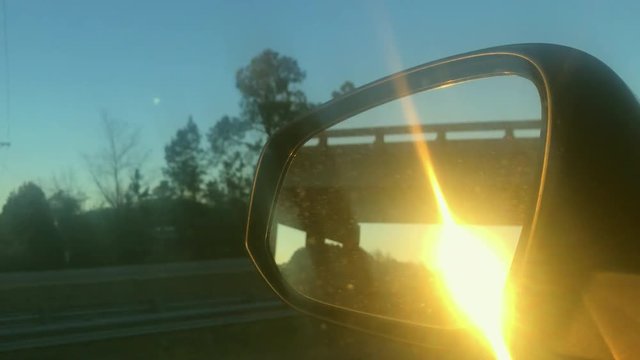 sunset in the rear view mirror of a rav4 car cruising on a clean highway