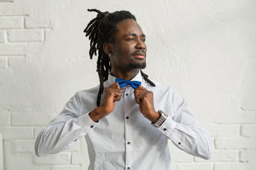 handsome african man with dreadlocks in a white shirt with a bowtie on a white background