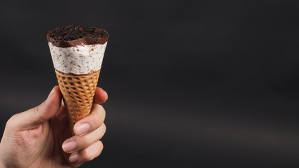 hand is holding ice cream cone with black background.