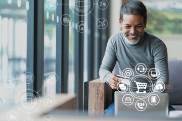 Asian or Hispanic man using Laptop and credit card payment shopping online with icon customer network connection on screen and connecting with omni channel system. Older man satisfied with CRM system