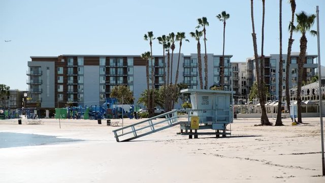 Mobile toilet washroom on the sandy calm beach of Santa Monica California with palm trees and apartments in the background
(wide shot)