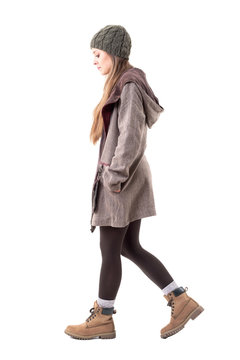 Side view of calm or sad hipster girl in winter warm clothes walking and looking down. Full body isolated on white background. 