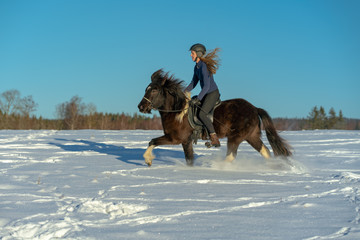 Young Swedish woman enjoying a ride on her Icelandic horse in deep snow