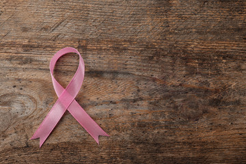 Pink ribbon on wooden background, top view with space for text. Breast cancer awareness concept
