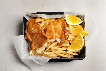 Container with British traditional fish and potato chips on light background, top view