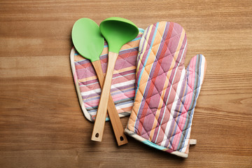 Soup ladle, spatula and potholders on wooden background, top view