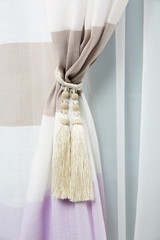 Beautiful draped window curtain with tieback in room, closeup