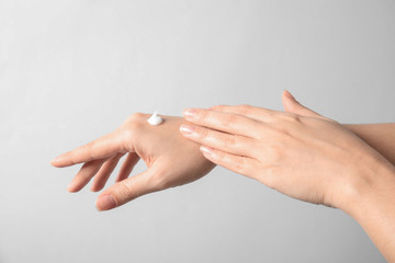 Woman applying hand cream on light background, closeup