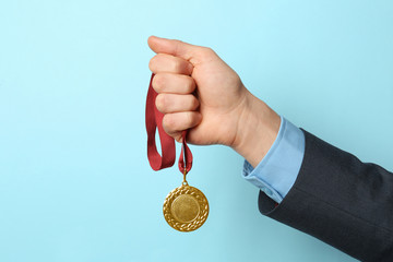Plakat Man holding golden medal on color background, closeup. Space for text