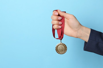Woman holding golden medal on color background, closeup. Space for text