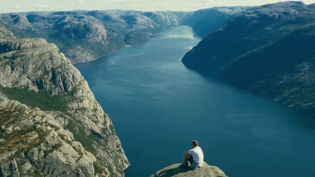 Man posing on the edge of Pulpit Rock, a cliff hundreds of meters above the seas of Lysefjord in Norway, people waiting for their turn to take a picture of them standing dangerously close to the edge