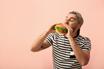 Young man eating tasty burger on color background. Space for text - obrazy, fototapety, plakaty