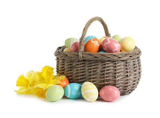 Wicker basket with painted Easter eggs and spring flowers on white background
