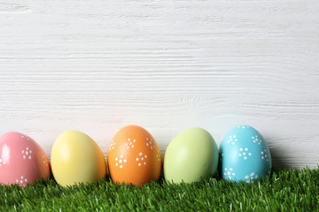 Colorful painted Easter eggs on green grass against wooden background, space for text