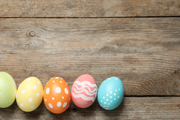 Flat lay composition of painted Easter eggs on wooden background, space for text