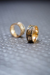 gold wedding rings with a pattern lie on a gray fabric