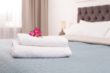 Stack of fresh towels with flowers on bed in hotel room