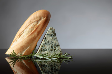Blue cheese with bread and rosemary on a  reflective background.
