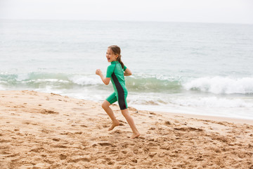 Fototapeta na wymiar Girl running on tropical beach, having fun, smiling, dressed in protective wetsuit.