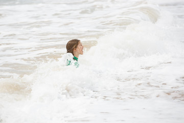 Girl playing in waves, having fun, dressed in protective wetsuit.