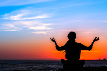 Silhouette of a yoga woman in a Lotus position on the ocean during a bloody red sunset.