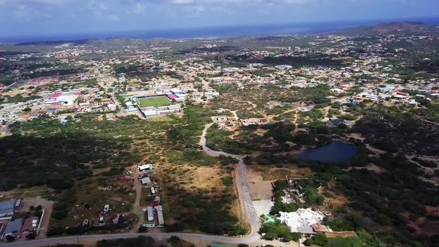 Aerial view of a natural lake and a tennis court in the centre of Aruba with the Caribbean Sea in the background.