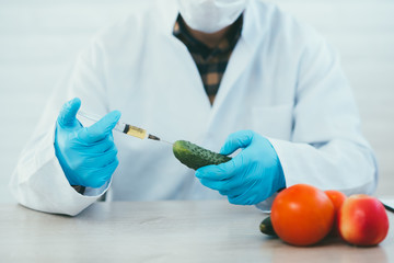 lab technician in lab coat and gloves colitis nitrates and GMO in cucumber on white background in...