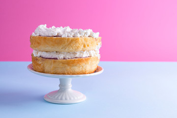 A festive sponge cake with white cream for a birthday, on a pink and blue background. Food for the holiday. Advertising poster and place for text. Copy cpace.