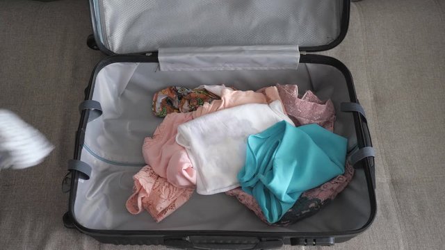 Lady quickly packs things. Packing luggage in a rush, top view