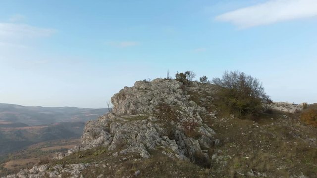 Tracking aerial shot over rocky hill, valley and forest as background