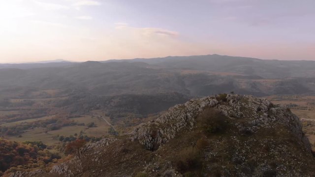 Tracking out aerial shot over rocky hill, valley and forest as background